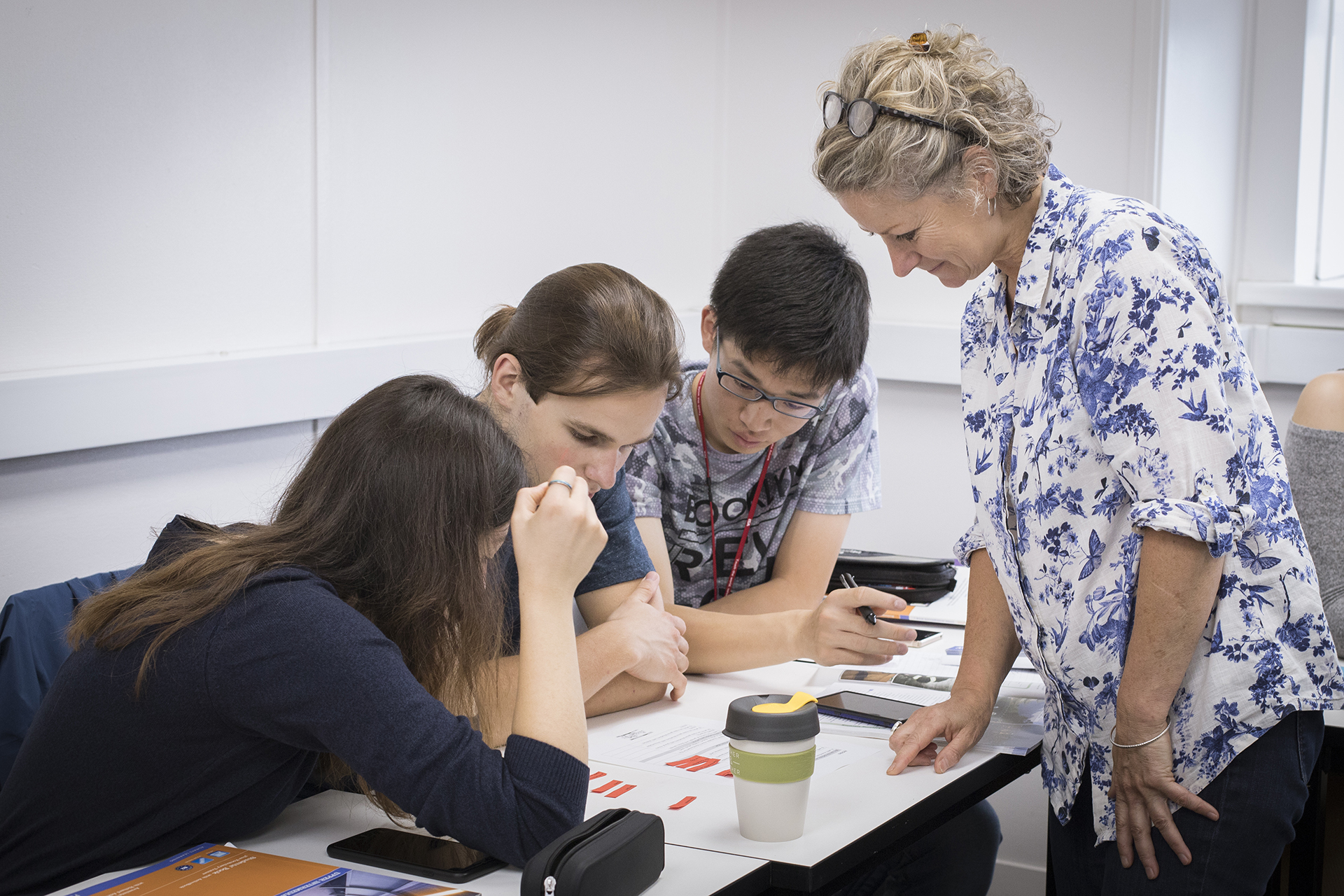 Teacher helping three students sitting at a desk with their work.