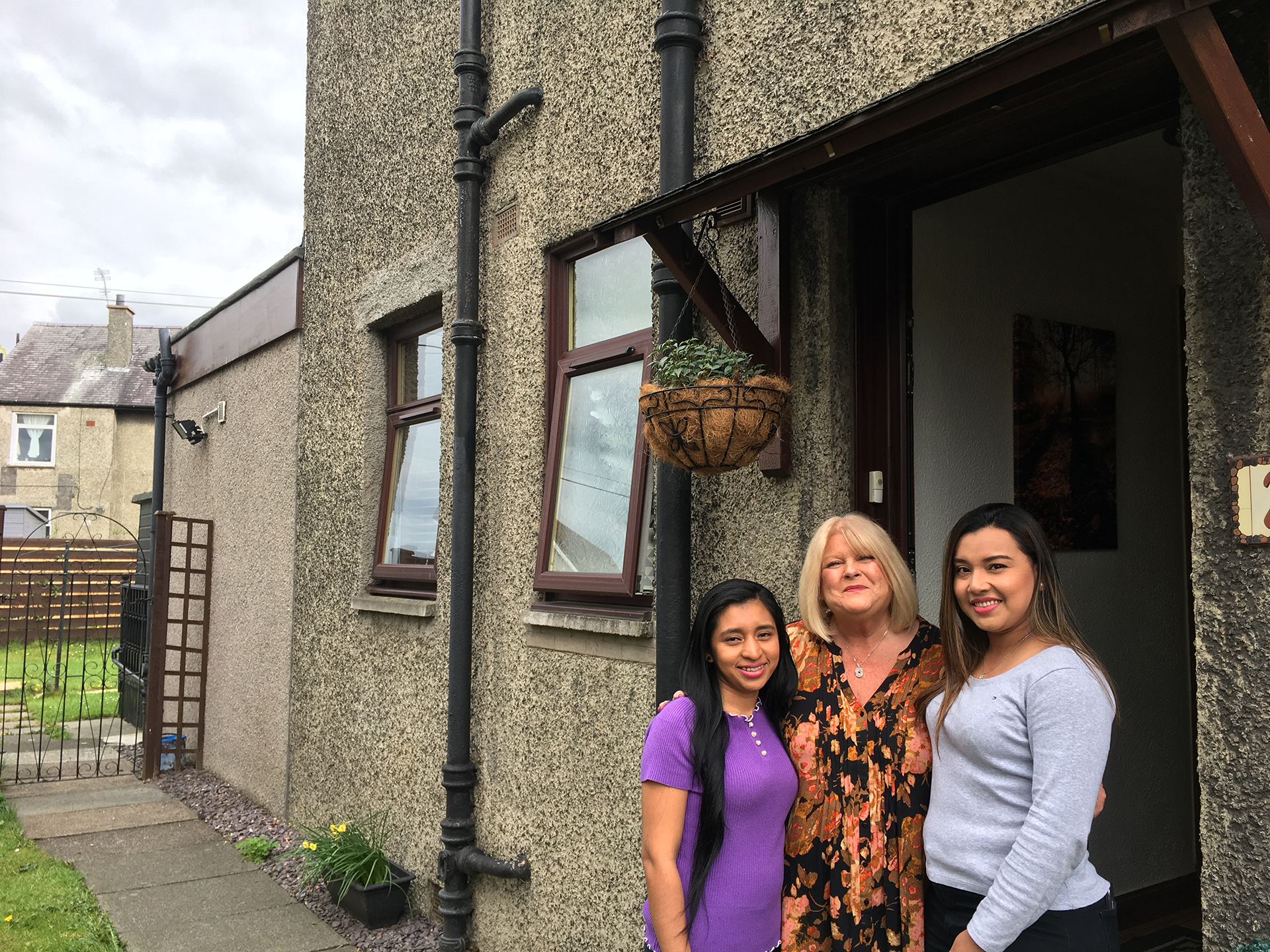 Two exchange students standing with their host outside a house.