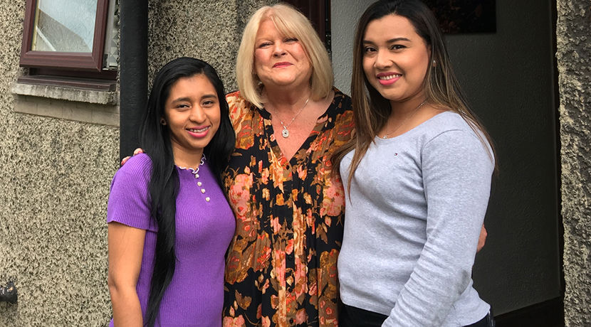 Two exchange students standing with their host outside a house.