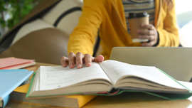 Person holding a coffee cup is holding open a page on a book. 