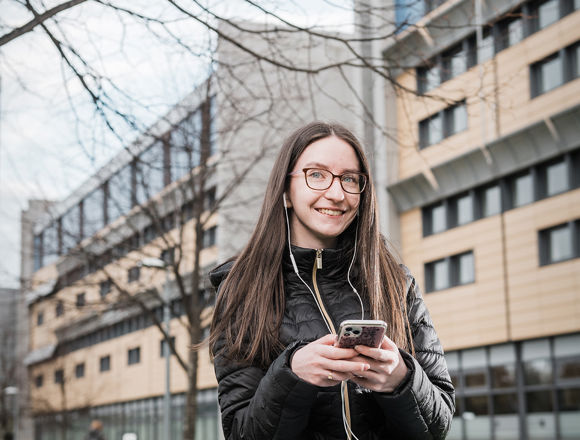Student sitting on the grass outside a campus building, looking at their phone.