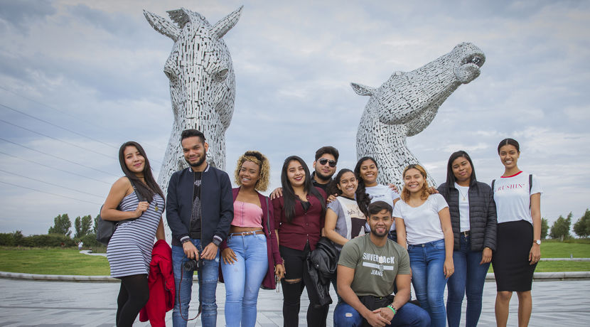 Group of students on a social programme standing for a group photo at the Kelpies, which are a large metal horse structure.