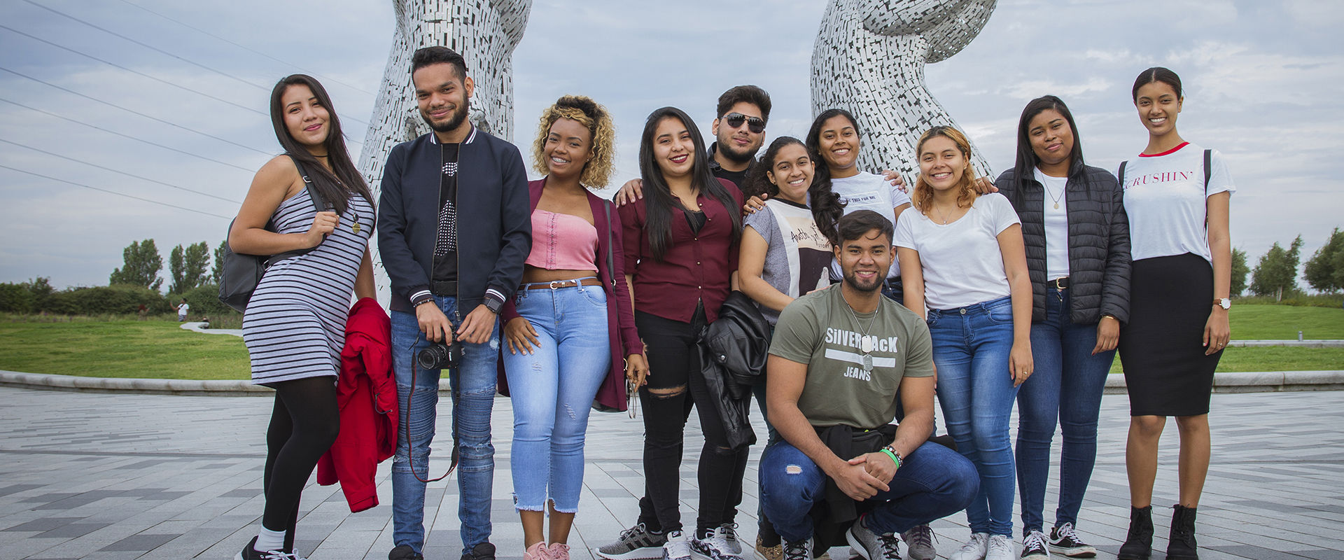 Group of students on a social programme standing for a group photo at the Kelpies, which are a large metal horse structure.