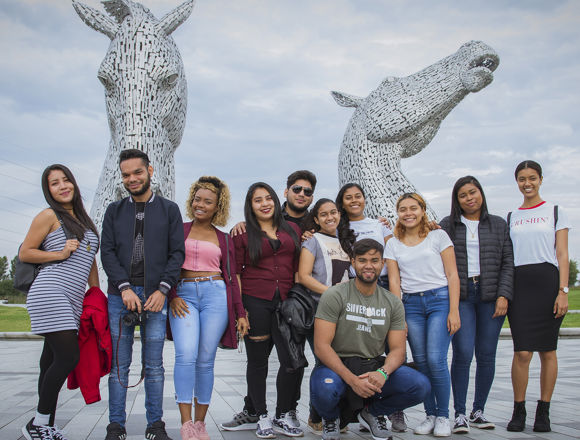 Group of students on a social programme standing for a group photo at the Kelpies, which are a large metal horse structure.