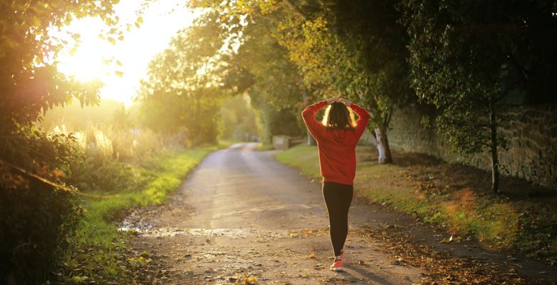 Person walking down a country road as the sun sets, surrounded by trees and nature.