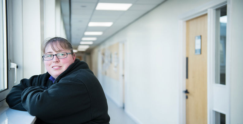 Smiling student leaning on a windowsill in a corridor.
