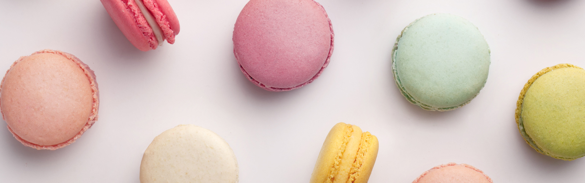 Macrons of various colours spread out on an off white background