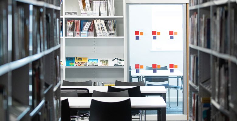 Book shelves in the library, with empty tables and chairs.
