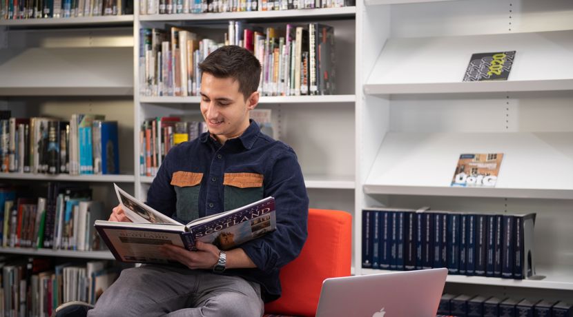 Young male student reading a book in the library.