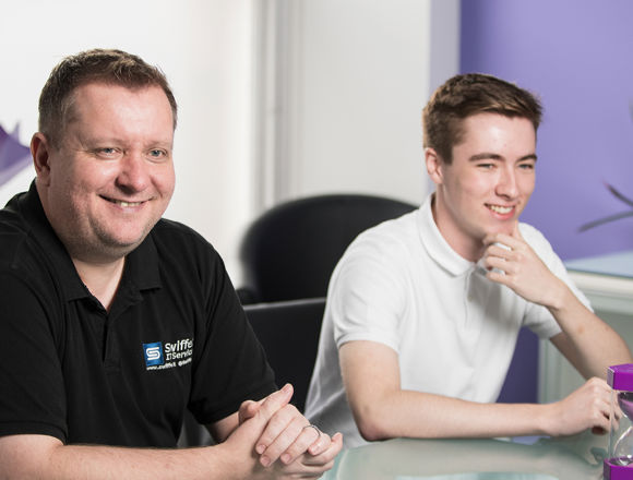 Young student working at a desk in an open plan office during a work placement next to their mentor.