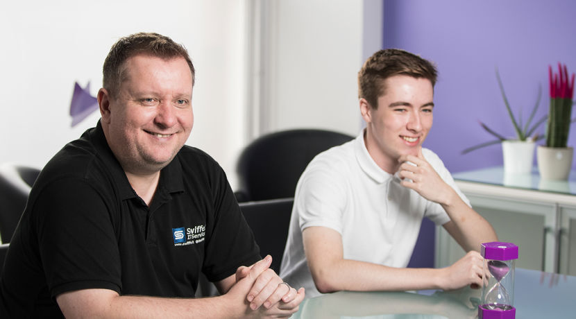 Young student working at a desk in an open plan office during a work placement next to their mentor.