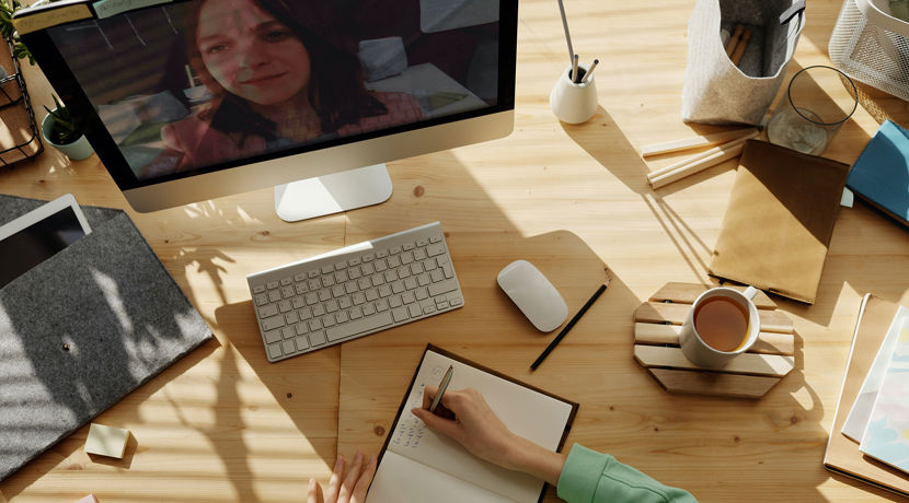 Person writing notes at their desk with their computer on and a cup of coffee next to them.