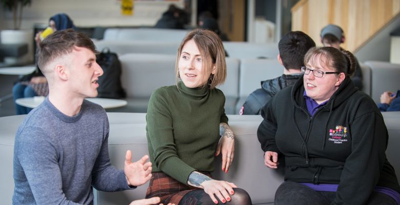 Three students having a conversation while sitting on a sofa at one of the college's communal areas.