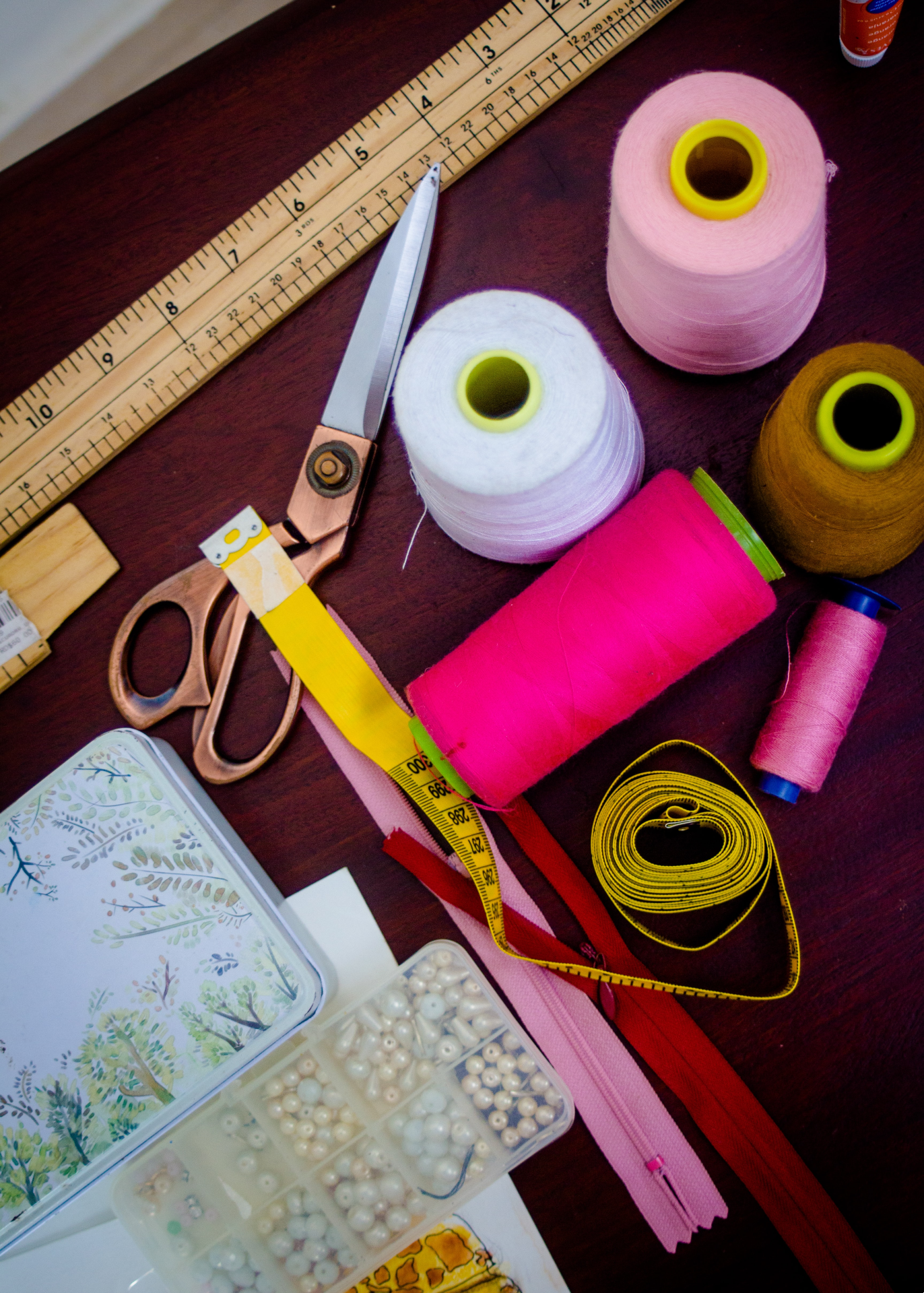 Sewing equipment on a desk. The equipment includes threads, scissors, beads and tape measures. 