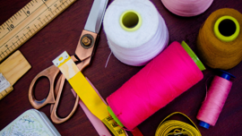 Sewing equipment on a desk. The equipment includes threads, scissors, beads and tape measures. 