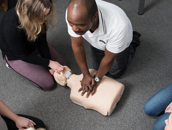 Health students learning CPR on a dummy in a classroom.