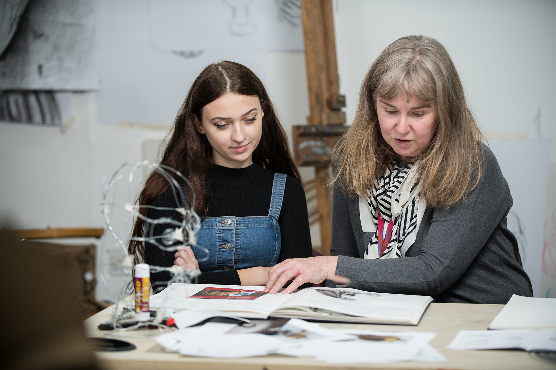 Lecturer helping a young student with their work in an art classroom.