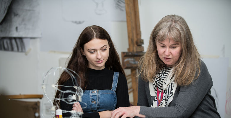 Lecturer helping a young student with their work in an art classroom.