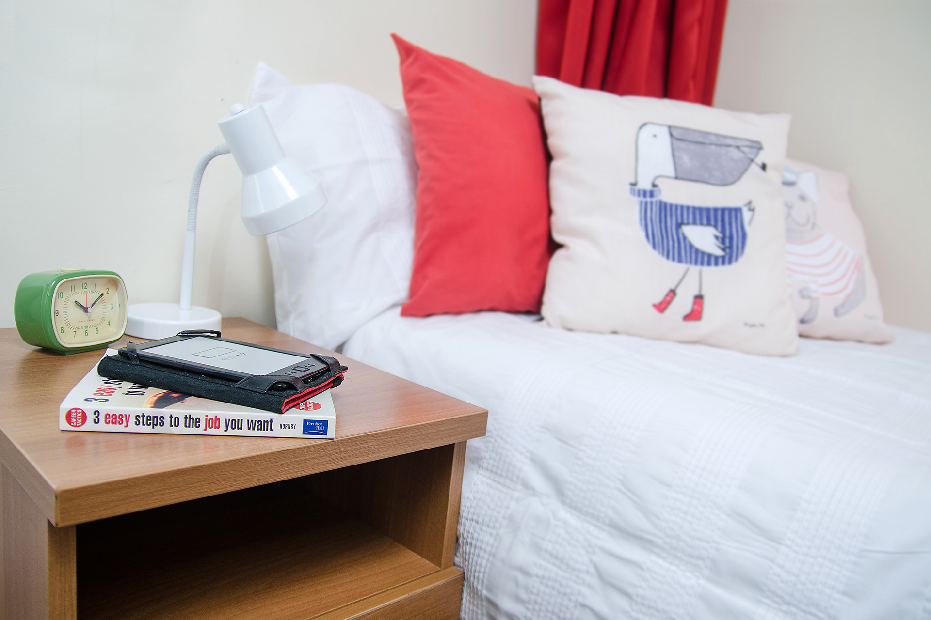 Alarm clock, book and lamp on a beside table in a student flat. 
