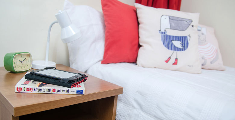 Alarm clock, book and lamp on a beside table in a student flat.