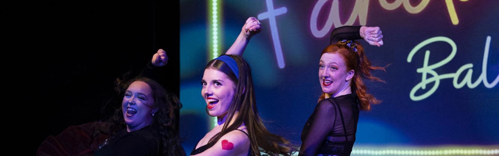 Three dancers perform on stage in colorful tutus, showcasing dynamic movement with a bright background that reads “Fandango Ballet.”