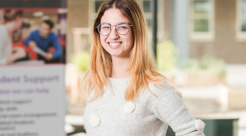 Smiling student wearing glasses in a college classroom.