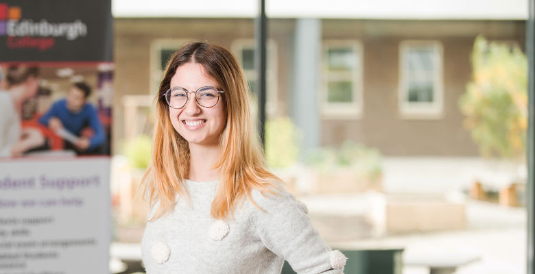 Smiling student wearing glasses in a college classroom.