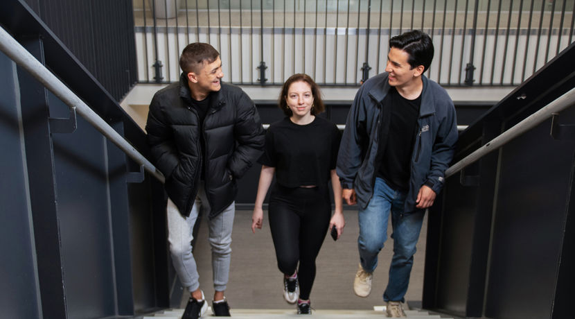 Three students talking and laughing with each other while walking up stairs at a college building.