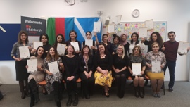 A group of diverse individuals proudly display their certificates, celebrating their achievements in front of a colorful backdrop.