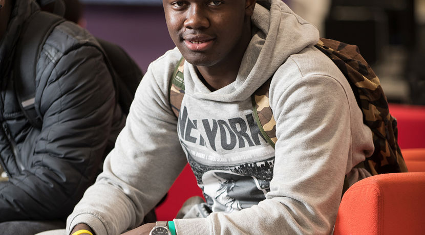 Young student sitting on a chair in a communal area at the college campus.