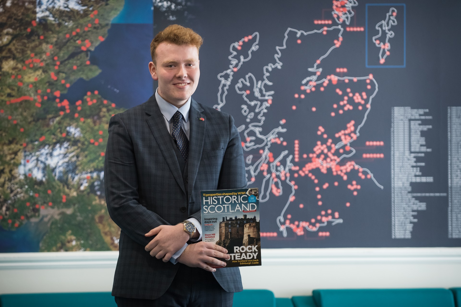 Young student wearing a suit, holding a Historic Scotland magazine at the front of a classroom. 