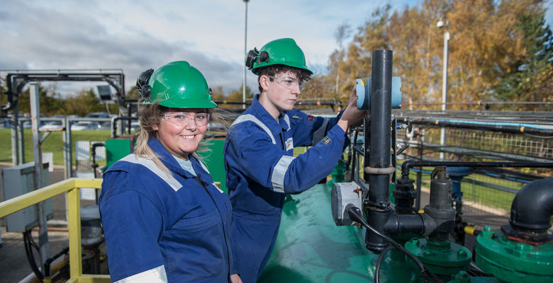 Two oil and gas students working away, both wearing blue boiler suit, hard hat and safety goggles.