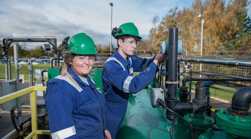 Two oil and gas students working away, both wearing blue boiler suit, hard hat and safety goggles.