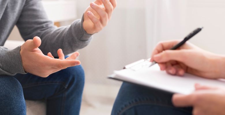 Close up of two people speaking during a counselling session. One person is taking notes on a notepad.