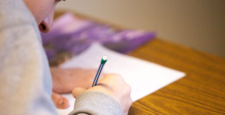 Person crouched over a desk writing on a piece of paper.