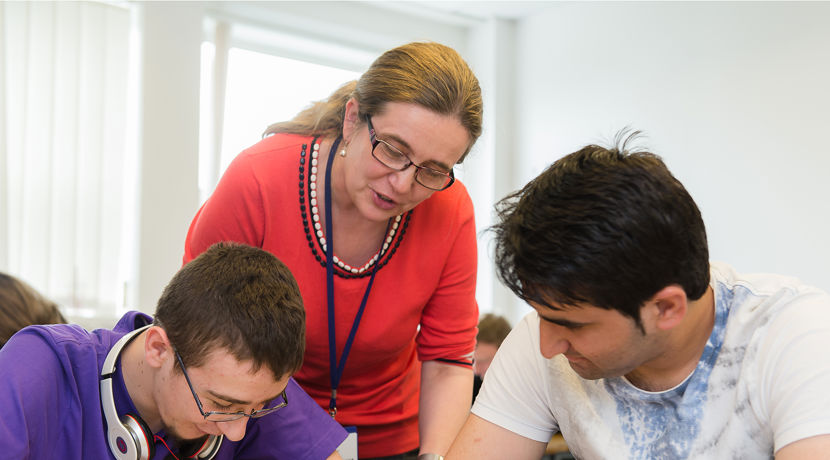 Lecturer supporting two students who are working in a classroom.
