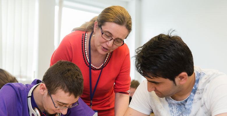 Lecturer supporting two students who are working in a classroom.