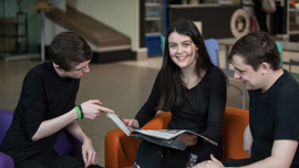 Three young students looking at a book together and discussing it.