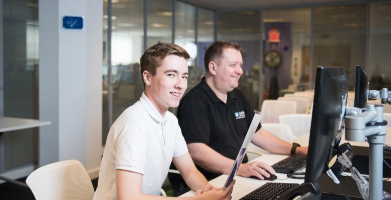 Young student working at a desk in an open plan office during a work placement.
