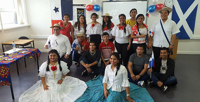 A group of individuals in colorful traditional clothing poses together in a room, showcasing cultural pride and community spirit.