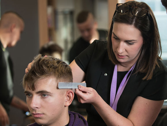 Lecturer is demonstrating a barbering technique to students.