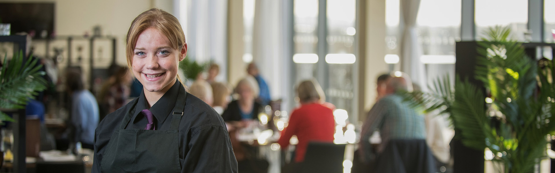 Hospitality student wearing black uniform working front of house in a busy restaurant.