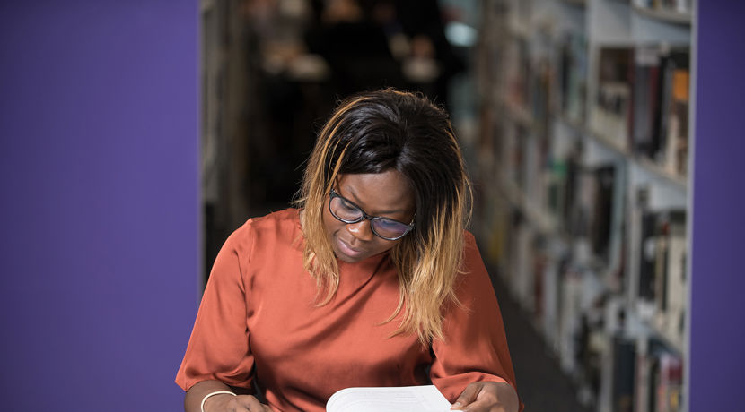 Student in the library reading a book at a desk.