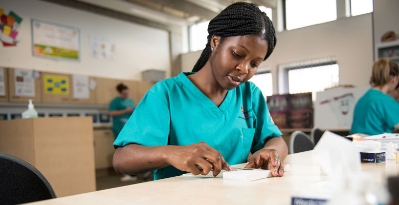 Dental student wearing blue scrubs working with dental tools at a desk.