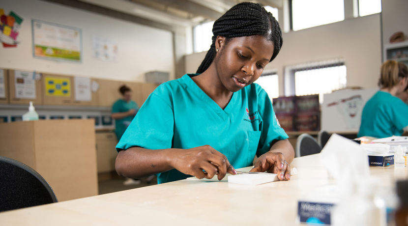 Dental student wearing blue scrubs working with dental tools at a desk.